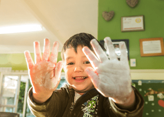 Boy holding hands covered in paint to the screen